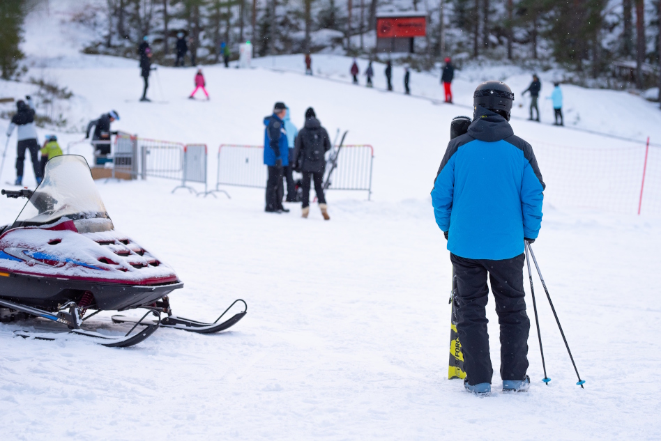 luminen maisema laskettelukeskuksesta, ihminen seisoo moottorikelkan vieressä