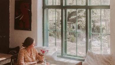 Nainen kahvittelee Cafe Mathildedalissa puisen pöydän äärellä ja katsoo ulos ikkunasta.