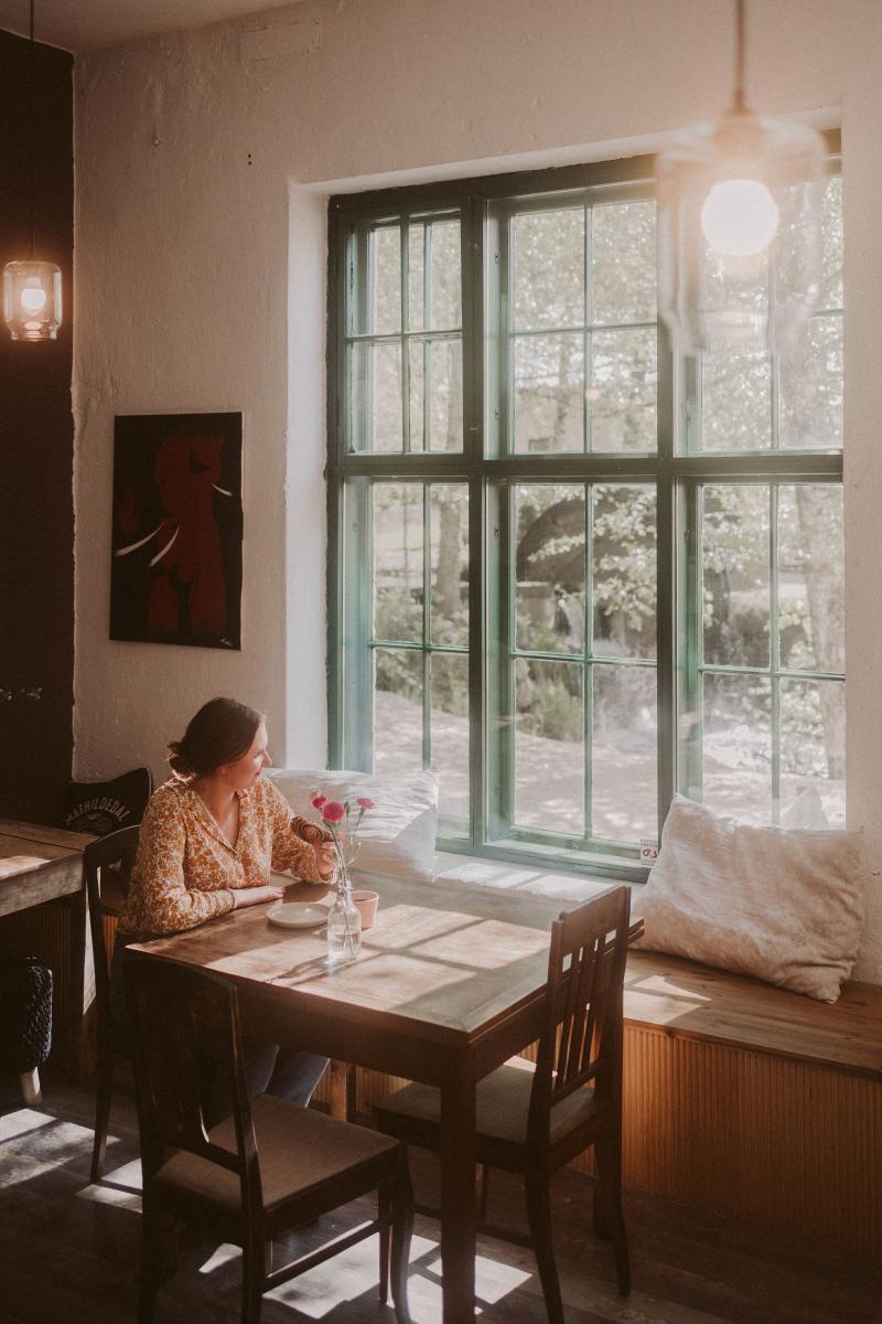 Nainen kahvittelee Cafe Mathildedalissa puisen pöydän äärellä ja katsoo ulos ikkunasta.